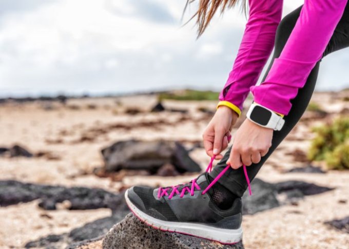 Biegająca kobieta w zegarku do biegania wiąże buta